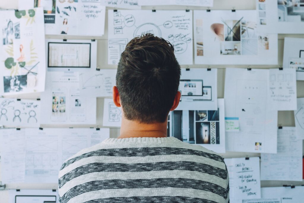 A man in a striped top stands with his back facing the camera, looking at a mood board, contemplating serviced offices vs leasehold offices