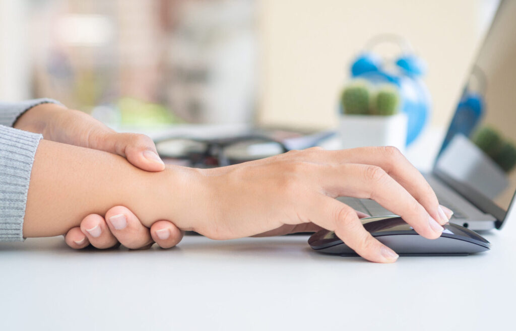 Closeup woman holding her wrist pain from using computer long time. Remote working discomfort from improper desk use.