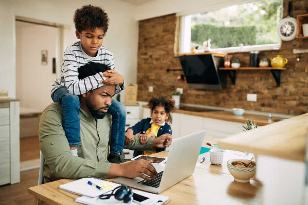 Father using laptop and working at home while being distracted by his small children.