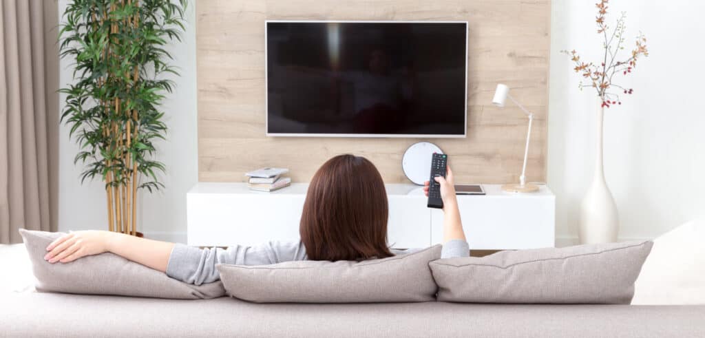 Young woman watching TV in the living room living a sedentary lifestyle