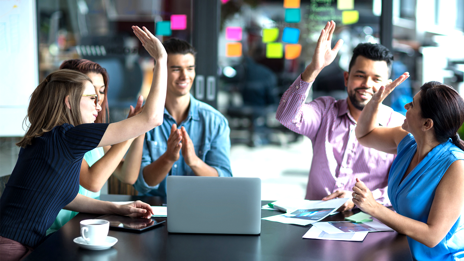 Team celebrates a business success by high fiving a colleague in a happy workplace