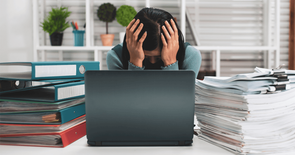 Woman suffering workplace stress due to the huge piles of papers and files that have been put on her desk to work through