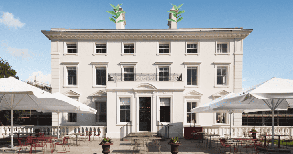 Beautifully restore winslade manor in the sunshine with parasols and tables on the terrace, the sign of scaffolding is visible in the background as the rest of the site continues to be renovated - 2020 Two leafy branches protrude from roof to represent sustainability