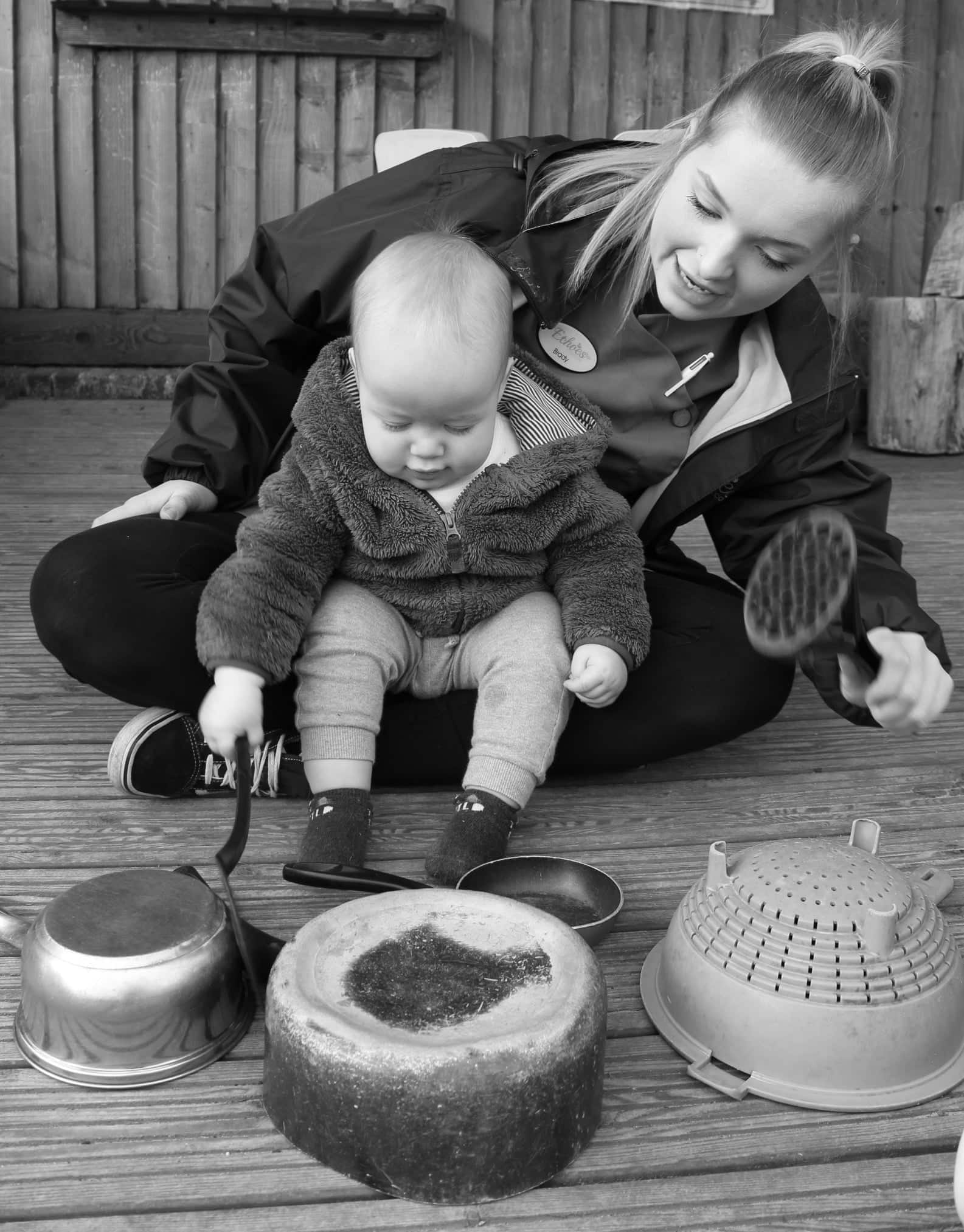 Staff member with baby sitting on lap playing with pots and pans