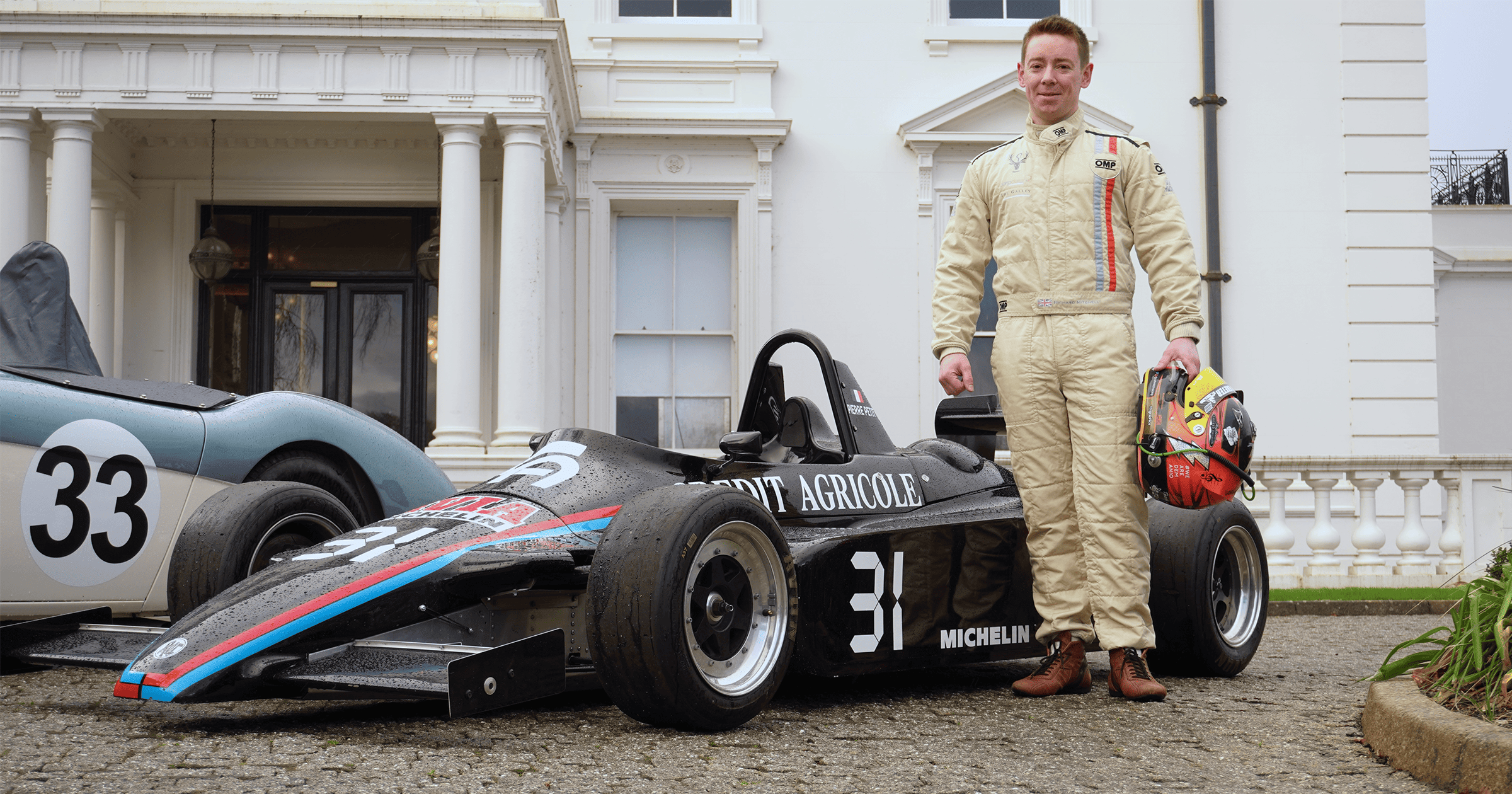 Richard Mitchell standing outside Winslade Manor with his Ensign Motorsports F3 car